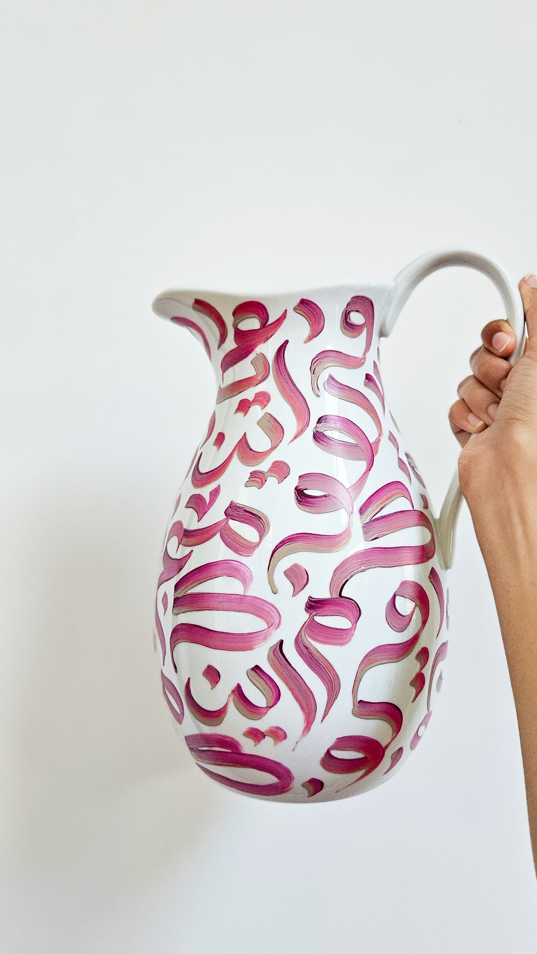 White pitcher with pink abstract patterns held by a hand against a white background